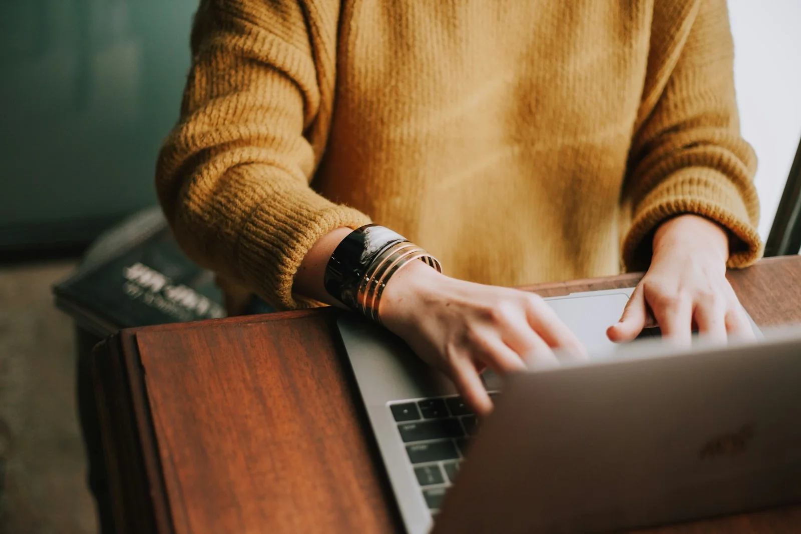 An adult researching on a laptop at a wooden table